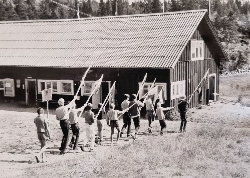 Barn tågar med fanor och flaggor mot storstugan